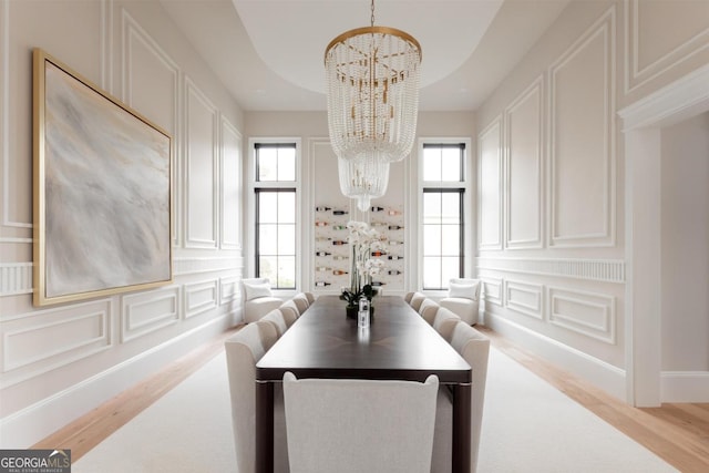 dining space with wood finished floors, a raised ceiling, a decorative wall, and an inviting chandelier