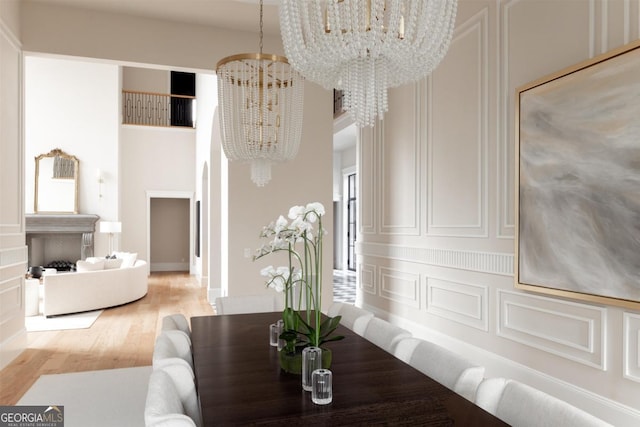 dining space with a towering ceiling, an inviting chandelier, a decorative wall, and wood finished floors