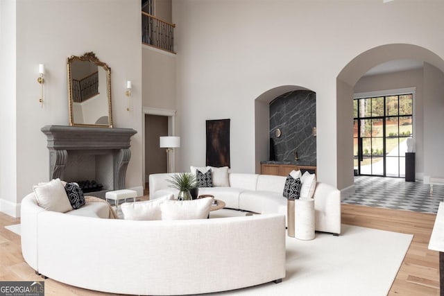 living room featuring arched walkways, a towering ceiling, baseboards, and wood finished floors