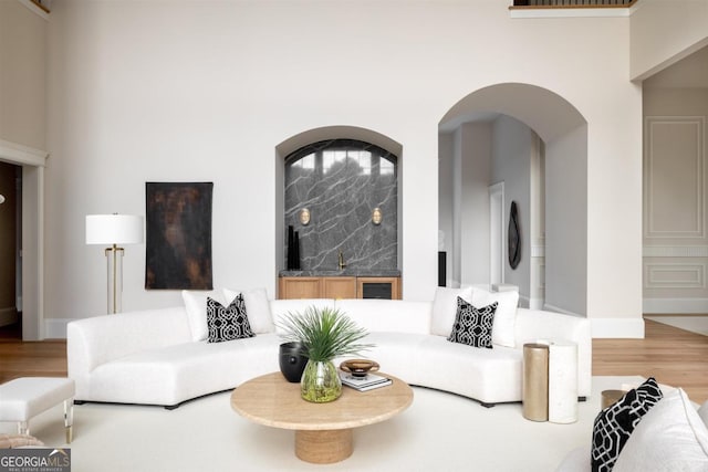 living area featuring arched walkways, a towering ceiling, wood finished floors, wet bar, and baseboards