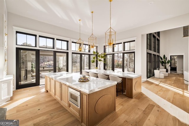 kitchen with a towering ceiling, light wood-type flooring, a center island, stainless steel microwave, and plenty of natural light