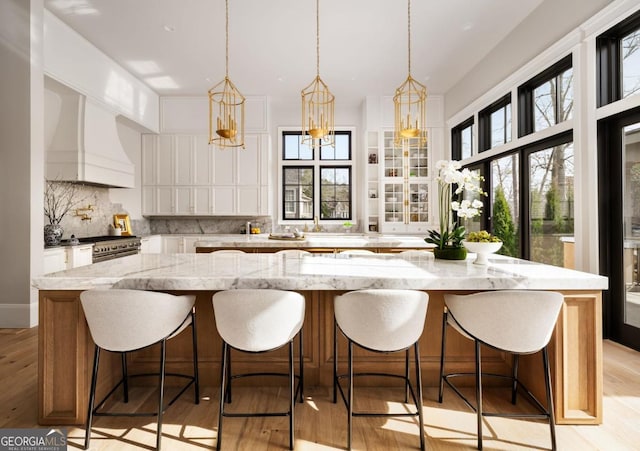 kitchen featuring light wood-style flooring, white cabinets, a large island, custom exhaust hood, and decorative backsplash