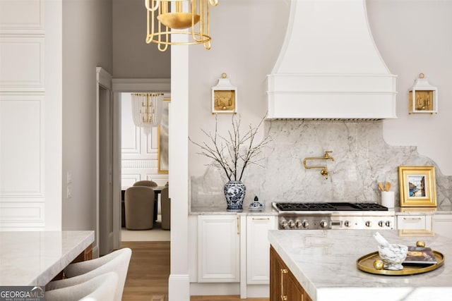 kitchen with light stone counters, tasteful backsplash, custom range hood, stainless steel gas stovetop, and white cabinetry