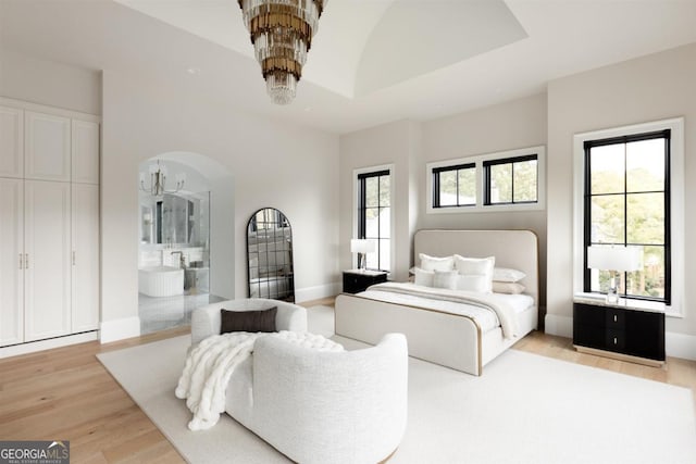 bedroom featuring baseboards, arched walkways, a tray ceiling, light wood-style floors, and a notable chandelier