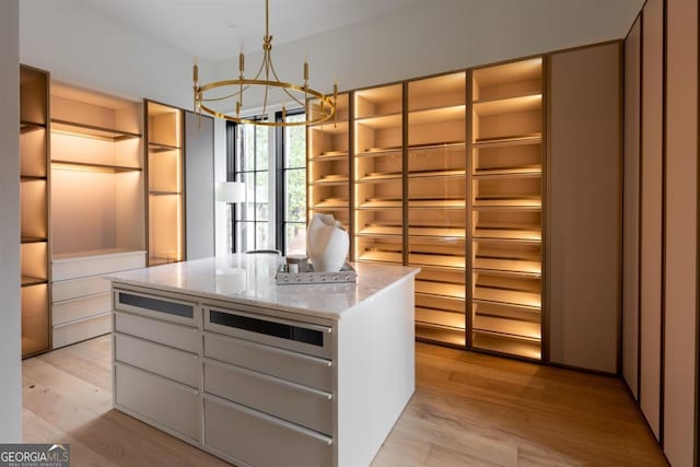 spacious closet with light wood-type flooring and an inviting chandelier