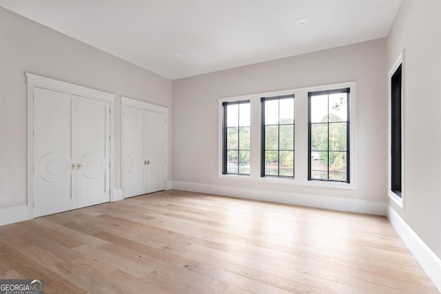 unfurnished bedroom featuring light wood-style flooring, baseboards, and two closets