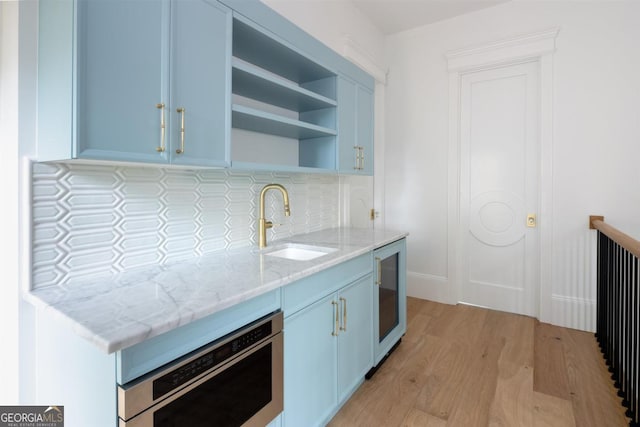 kitchen featuring open shelves, light wood-type flooring, a sink, and blue cabinets