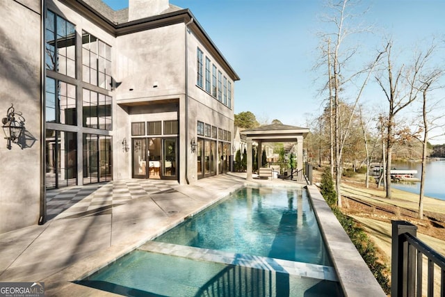 rear view of property with a chimney, a gazebo, a patio area, a pool with connected hot tub, and stucco siding