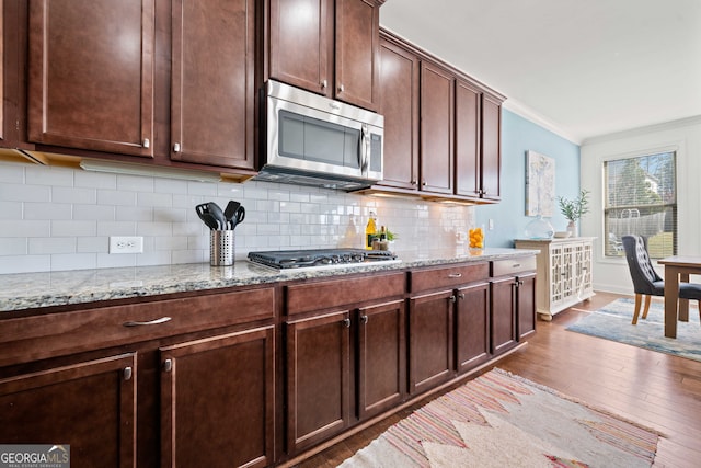 kitchen featuring dark wood-type flooring, ornamental molding, tasteful backsplash, stainless steel appliances, and light stone countertops