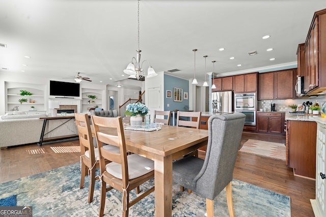 dining area with built in features, visible vents, a fireplace, dark wood-type flooring, and crown molding