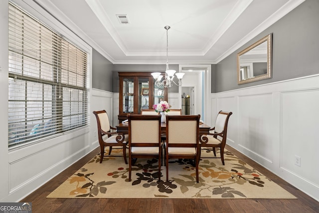 dining space featuring visible vents, a tray ceiling, wood finished floors, an inviting chandelier, and a decorative wall