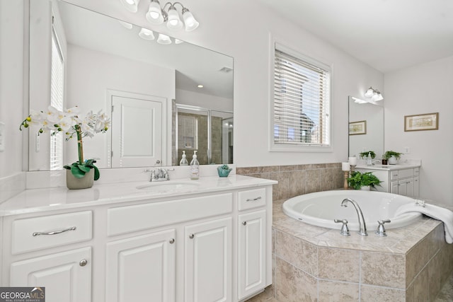 full bath with visible vents, two vanities, a stall shower, a bath, and a sink