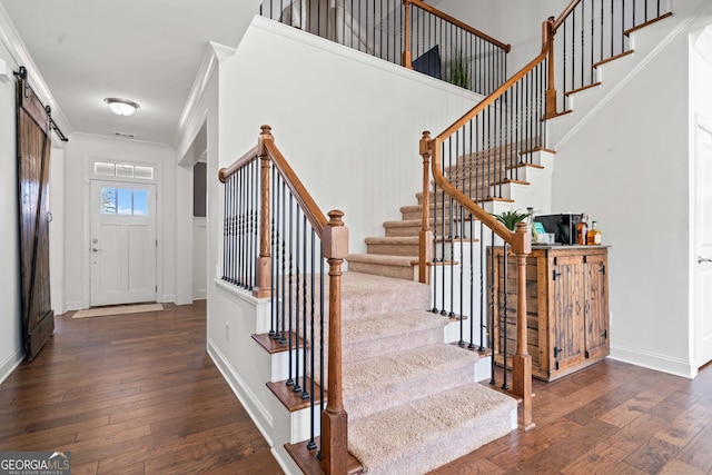 stairs with hardwood / wood-style floors, a barn door, baseboards, and ornamental molding