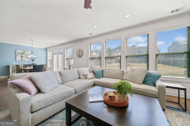 living room with visible vents, baseboards, ornamental molding, an inviting chandelier, and wood finished floors