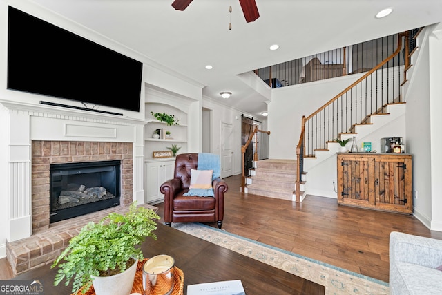 living area with built in shelves, ceiling fan, stairs, hardwood / wood-style floors, and a fireplace