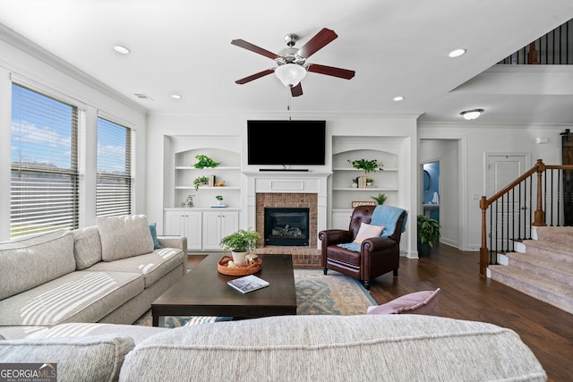 living area with ornamental molding, built in features, wood finished floors, stairway, and a fireplace