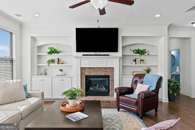 living room featuring built in features, wood finished floors, visible vents, ornamental molding, and a brick fireplace