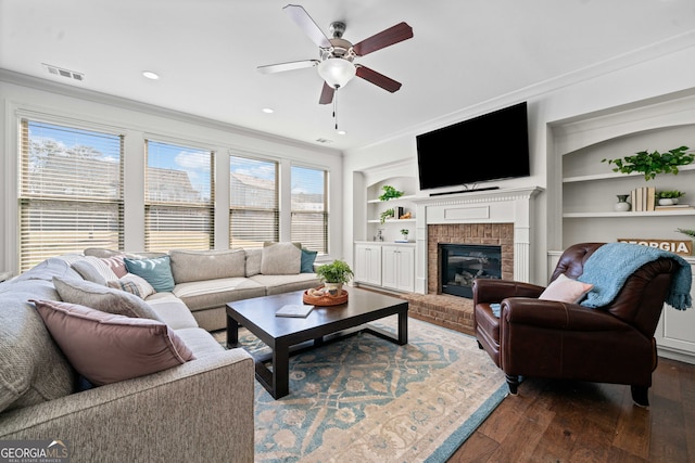 living area with visible vents, ornamental molding, built in features, dark wood finished floors, and a fireplace