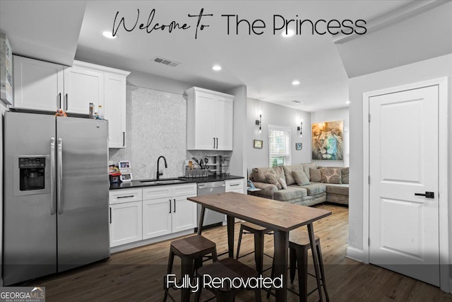 kitchen featuring stainless steel appliances, dark wood-type flooring, a sink, tasteful backsplash, and dark countertops