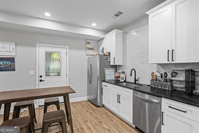 kitchen with a sink, visible vents, appliances with stainless steel finishes, light wood-type flooring, and decorative backsplash