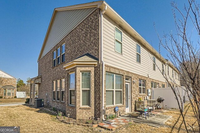 exterior space with central AC unit, a patio area, fence, and brick siding