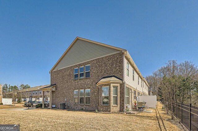 view of side of property with central air condition unit, brick siding, fence, and a lawn