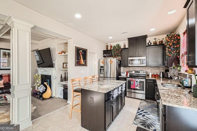 kitchen featuring a fireplace, visible vents, appliances with stainless steel finishes, a sink, and a kitchen bar