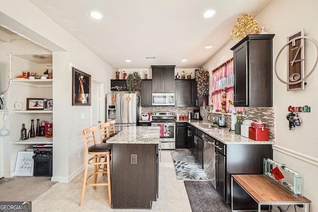 kitchen with decorative backsplash, a kitchen island, light stone counters, stainless steel appliances, and a kitchen bar