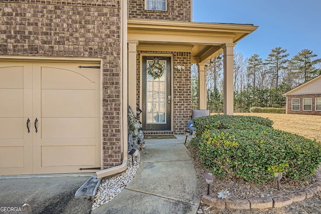 view of exterior entry with covered porch, brick siding, and an attached garage