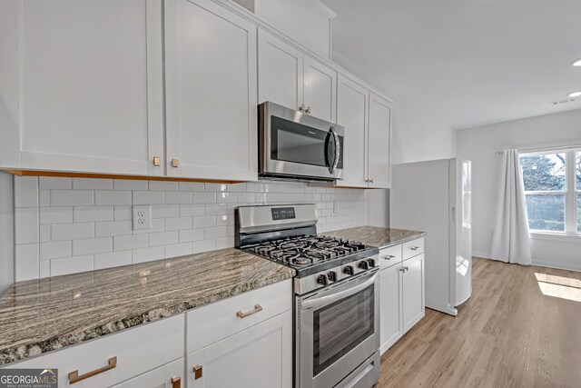 kitchen with light stone counters, stainless steel appliances, white cabinetry, light wood finished floors, and tasteful backsplash