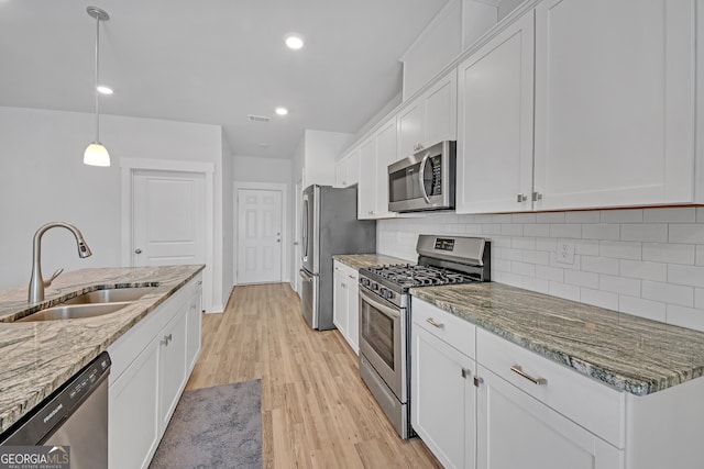 kitchen featuring tasteful backsplash, light wood-style flooring, appliances with stainless steel finishes, white cabinetry, and a sink