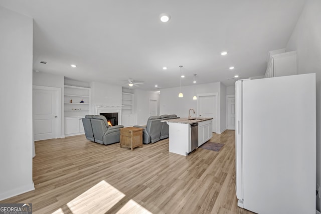 kitchen with a glass covered fireplace, open floor plan, freestanding refrigerator, white cabinetry, and a sink