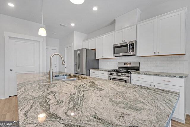 kitchen featuring stainless steel appliances, a sink, visible vents, light wood-type flooring, and tasteful backsplash