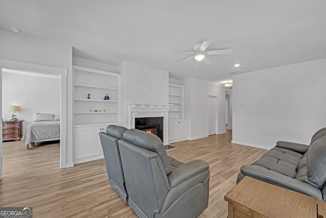 living room featuring visible vents, light wood-style flooring, a premium fireplace, ceiling fan, and baseboards