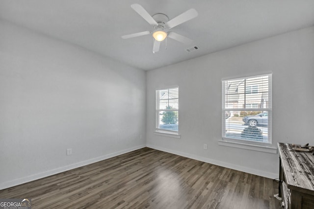 unfurnished room featuring dark wood-style floors, baseboards, visible vents, and a ceiling fan