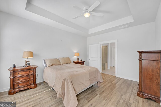 bedroom with light wood finished floors, a tray ceiling, visible vents, and baseboards