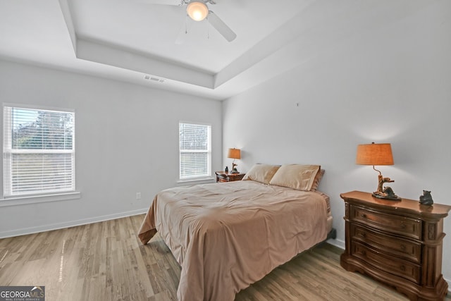 bedroom with light wood-type flooring, multiple windows, and a tray ceiling