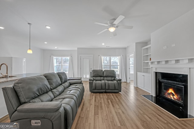 living room with a fireplace with flush hearth, ceiling fan, light wood-style floors, built in shelves, and recessed lighting