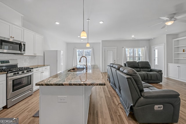 kitchen with appliances with stainless steel finishes, stone countertops, open floor plan, white cabinets, and a sink