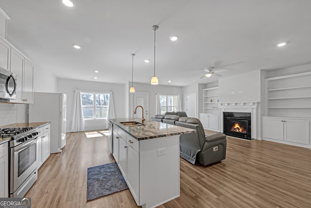 kitchen featuring light wood-style flooring, a sink, appliances with stainless steel finishes, dark stone countertops, and a glass covered fireplace