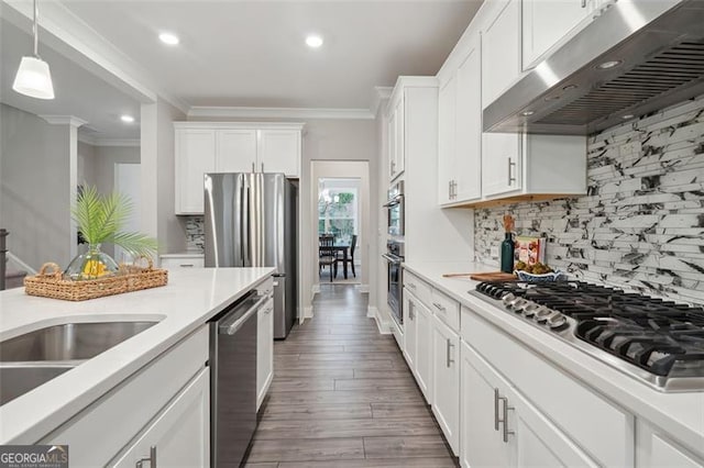 kitchen with range hood, light countertops, appliances with stainless steel finishes, ornamental molding, and white cabinetry