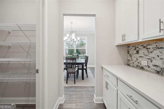 bar featuring backsplash, an inviting chandelier, ornamental molding, wood finished floors, and baseboards