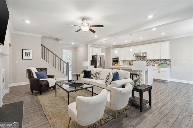 living room with a fireplace with flush hearth, crown molding, light wood-style flooring, and stairs