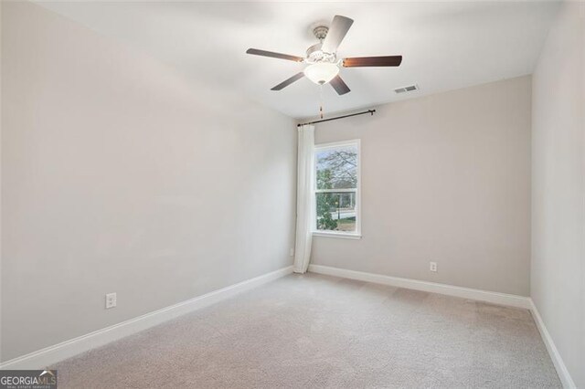 carpeted spare room with a ceiling fan, visible vents, and baseboards