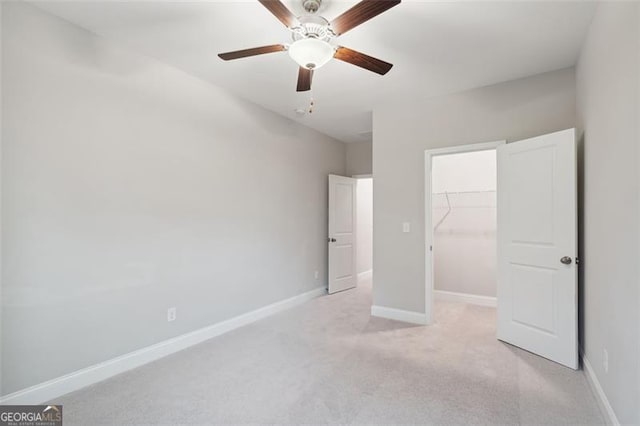 unfurnished bedroom with light carpet, a ceiling fan, baseboards, a spacious closet, and a closet