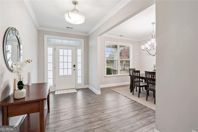 entryway featuring a notable chandelier, wood finished floors, visible vents, baseboards, and ornamental molding