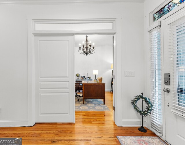 entrance foyer with ornamental molding, baseboards, light wood-type flooring, and a chandelier