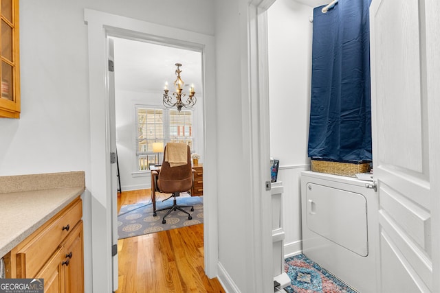 clothes washing area featuring light wood-type flooring, laundry area, washer / dryer, wainscoting, and a notable chandelier