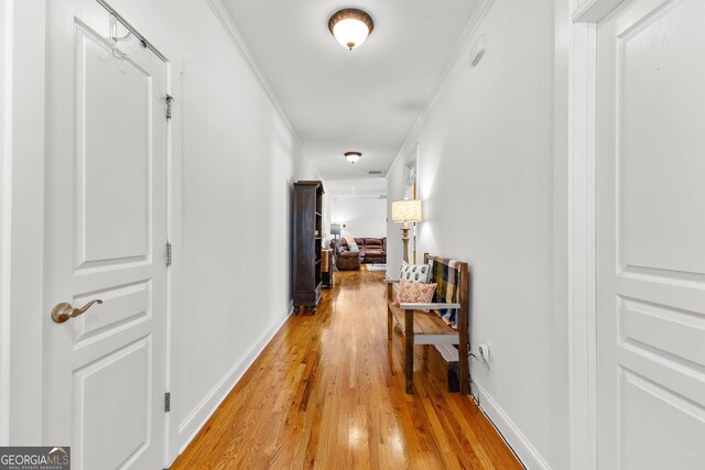 hallway featuring light wood-style flooring, baseboards, and ornamental molding