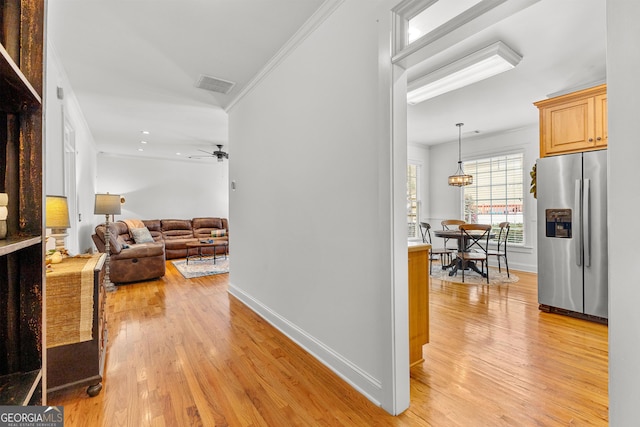 corridor with light wood-style flooring, baseboards, visible vents, and ornamental molding